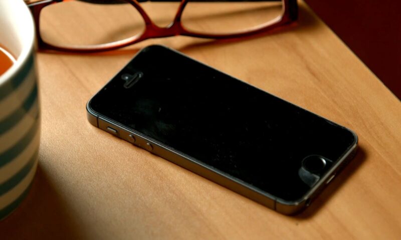 prikaz telefona, šolje sa čajem i naočara na drvenom stolu